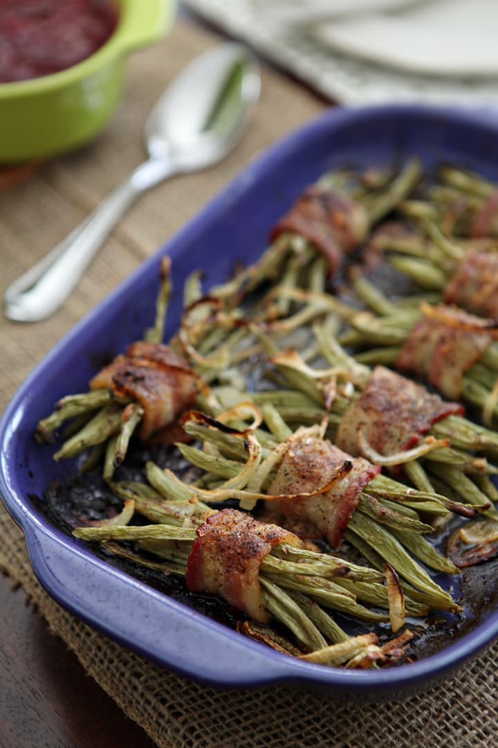 Green beans wrapped in bacon in blue baking dish 
